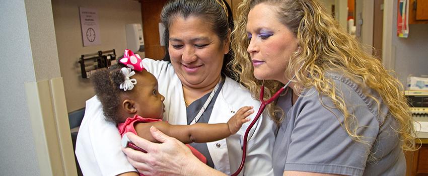 一名护士抱着婴儿，另一名护士在听婴儿的胸部