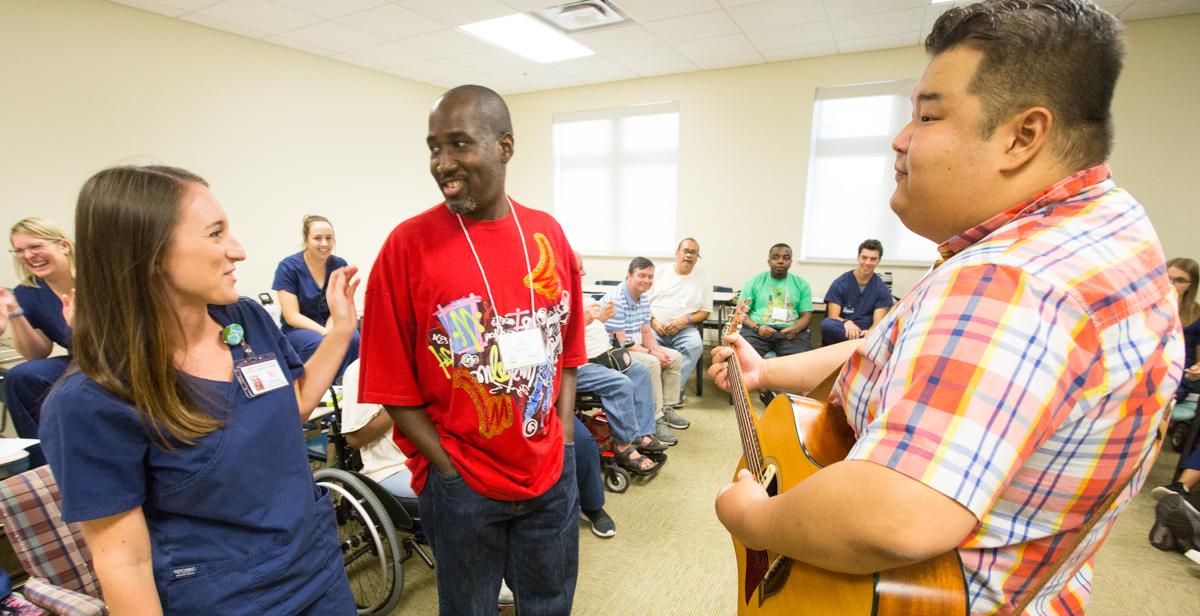 Kelsey总值, University of 南 Alabama speech-language pathology graduate student, assists traumatic brain injury camp participant Larry Malone Jr., center, while music therapist Fred Ra leads Malone and other camp participants in creating a song using words suggested by the group.
